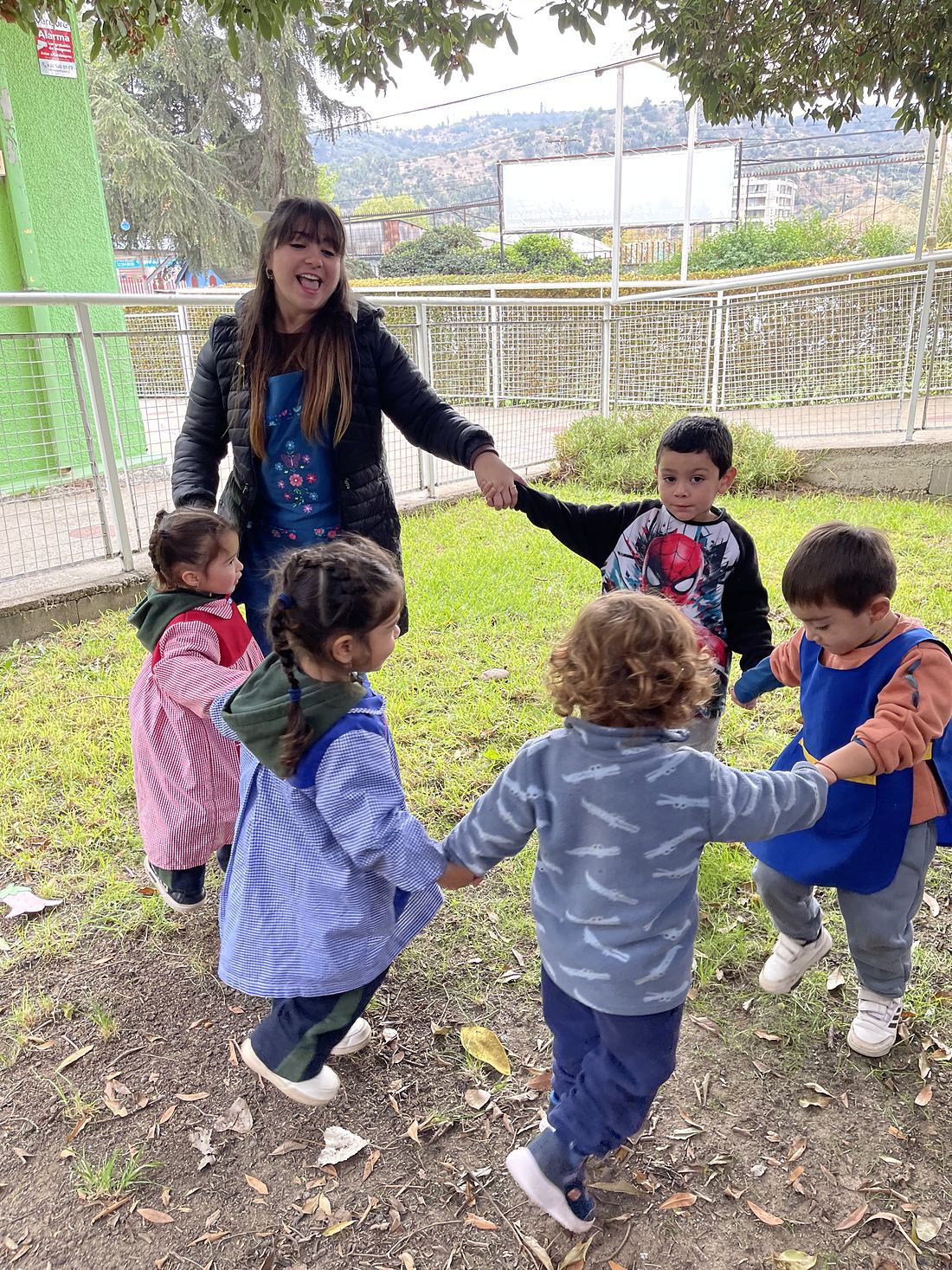 Educadora y párvulos jugando en ronda en el patio de la escuela
