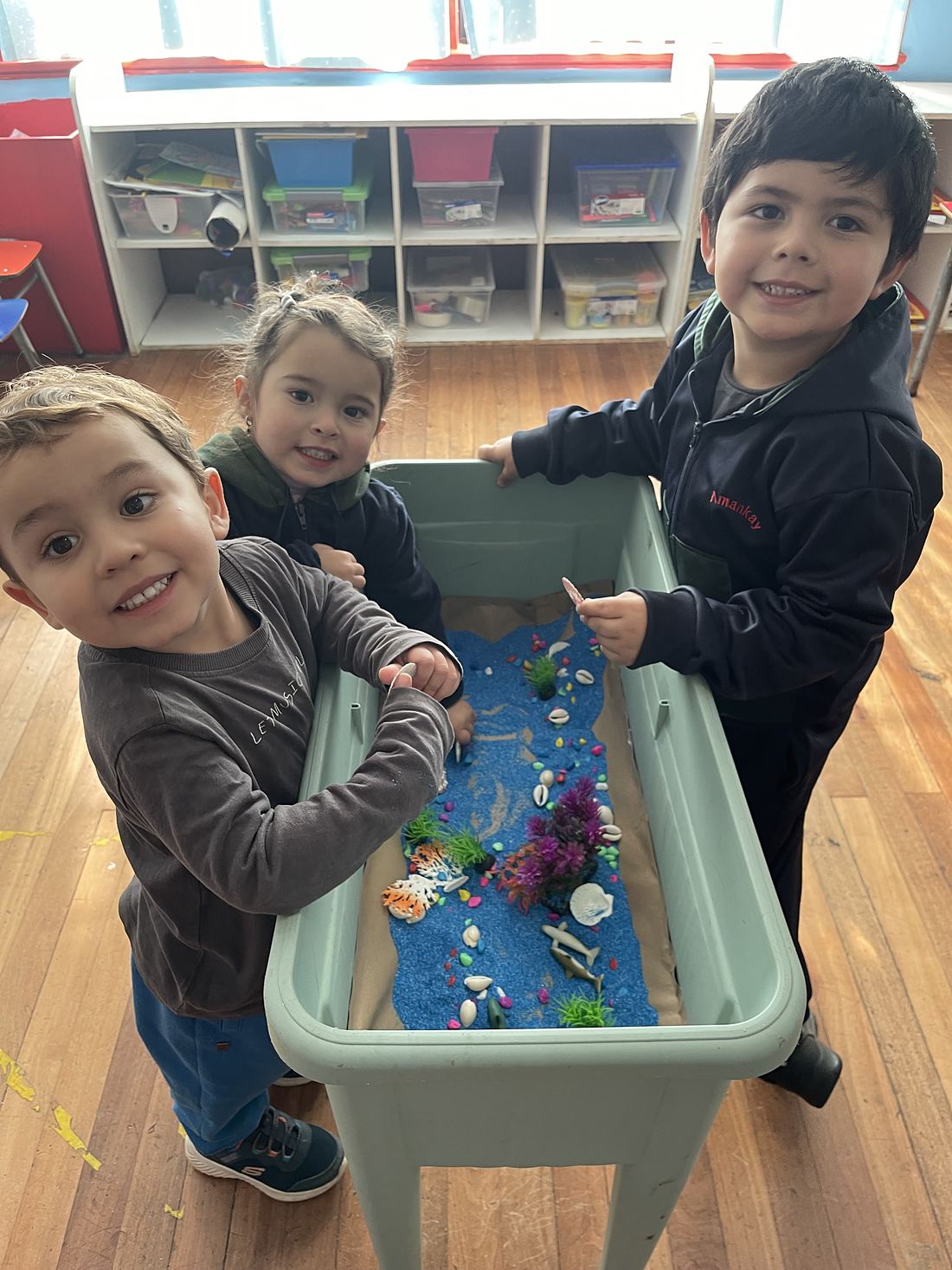 Dos niños exploran una mesa sensorial con agua y figuras marinas